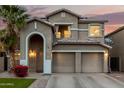Two-story home featuring a three-car garage, desert landscaping, and an arched entryway at dusk at 3882 W Goldmine Mountain Dr, San Tan Valley, AZ 85144