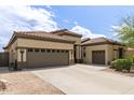 View of the tan home's three-car garage with a wide driveway and desert landscaping at 27315 N 83Rd Dr, Peoria, AZ 85383