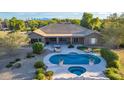 Aerial view of an inviting backyard featuring a sparkling pool, spa, lounging area, mature trees and mountain views at 14022 W Hope Dr, Surprise, AZ 85379
