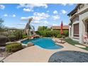 Backyard features pool with tropical landscaping, rock waterfall, a red umbrella, and outdoor seating area at 9843 E Acacia Dr, Scottsdale, AZ 85260