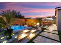 Inviting backyard with a pool, spa, outdoor kitchen, fire pit, and covered patio at dusk at 32268 N 133Rd Ln, Peoria, AZ 85383