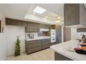 Well-lit kitchen with tile floors, a skylight, dark wood cabinets, and white countertops and breakfast bar at 11113 W Cameo Dr, Sun City, AZ 85351