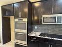 Modern kitchen featuring stainless steel double ovens, dark cabinetry, and granite countertops at 6506 S 50Th Ln, Laveen, AZ 85339