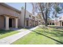 A tan, two-story apartment complex with trees and green lawn under a clear blue sky at 7126 N 19Th Ave # 122, Phoenix, AZ 85021