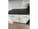 Close-up of a sleek, black countertop with white cabinets, subway tile backsplash and modern silver hardware at 16996 W Fetlock Trl, Surprise, AZ 85387