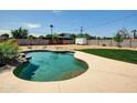 Backyard pool with rock waterfall feature, lush landscaping, and expansive concrete patio at 4337 E Wilshire Dr, Phoenix, AZ 85008