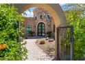 Charming home exterior features a stone tower, complemented by a brick walkway framed by mature desert landscaping and an arched gate at 37334 N Winding Wash Trl, Carefree, AZ 85377