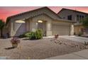 Well-maintained single-story home with a two-car garage and desert landscaping under a pink sky at 44284 W Buckhorn Trl, Maricopa, AZ 85138