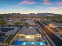 An aerial view of a house and neighborhood with pool and mountain views at dusk at 11934 S 181St Ave, Goodyear, AZ 85338