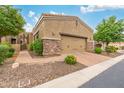 View of the two-car garage featuring a neutral stucco exterior, stone accents, a brick paver driveway, and manicured landscaping at 6202 E Mckellips Rd # 189, Mesa, AZ 85215