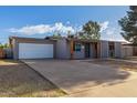 Single story grey home with front lawn and long driveway to attached garage at 3021 E Larkspur Dr, Phoenix, AZ 85032