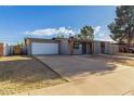 Single story grey home with front lawn and long driveway to attached garage at 3021 E Larkspur Dr, Phoenix, AZ 85032