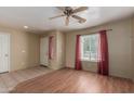Bright living room with wood-look flooring, neutral walls, ceiling fan and a large window with red drapes at 2122 W Alta Vista Rd, Phoenix, AZ 85041