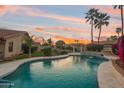 Backyard pool with a rock waterfall feature, covered seating area, and lush landscaping at sunset at 1150 W Sherri Dr, Gilbert, AZ 85233