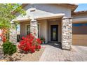 Inviting entryway with a decorative front door, stone pillars, and vibrant red flowers, creating a welcoming atmosphere at 18129 N 65Th Pl, Phoenix, AZ 85054