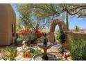 Beautiful garden featuring a stone arch, blooming plants, mature trees, and a charming fountain at 28045 N 112Th Pl, Scottsdale, AZ 85262