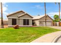 Inviting home featuring a lush green lawn, mature palm trees, desert rock landscaping, and charming architectural details at 6577 W Abraham Ln, Glendale, AZ 85308