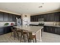 Modern kitchen features dark cabinets, stainless appliances, and a large center island with barstool seating at 20181 W Desert Bloom St, Buckeye, AZ 85326