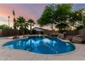 Sparkling pool with rock waterfall feature, lush trees, and ambient string lights for evening relaxation at 3152 N 83Rd Pl, Scottsdale, AZ 85251