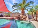 Backyard pool featuring an eye-catching rock waterfall, lush palm trees, and a stylish sunshade at 16322 N 171St Dr, Surprise, AZ 85388