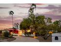 Desert home with a circular driveway, lush landscape, and a warm glow from the interior lights at 10380 E Cholla St, Scottsdale, AZ 85260