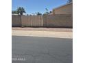 View of the sidewalk, street, brick wall, and wooden fence with palm trees in the distance at 5139 E Tano St, Phoenix, AZ 85044