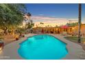 Backyard pool area featuring a sparkling pool, covered patio, string lights, lush greenery, and mature trees at 5837 E Presidio Rd, Scottsdale, AZ 85254