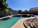 Inviting backyard pool featuring rock accents, lush landscaping, and ample space for relaxing under the sun at 14282 W Indianola Ave, Goodyear, AZ 85395