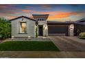 Charming single-story home at dusk with manicured lawn, stone accents, and a brick-paved driveway leading to a two-car garage at 17168 W Mountainair St, Surprise, AZ 85388