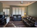 Inviting living room with comfortable leather sofas, ceiling fan, and shuttered windows offering ample sunlight at 20376 N Coronado Way, Surprise, AZ 85374