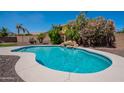 Sparkling pool with rock waterfall feature surrounded by lush landscaping and a privacy fence at 3574 E Glacier Pl, Chandler, AZ 85249