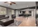 Spacious living room features a gray sectional sofa, ottoman, a view into dining area and tile flooring at 44468 W Eddie Way, Maricopa, AZ 85138