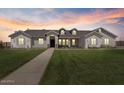 Charming one-story home features a well-maintained lawn, stone accents, and dormer windows during a picturesque sunset at 18826 E Augusta Ave, Queen Creek, AZ 85142