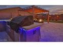 Backyard kitchen island with grill, bar seating and decorative blue lights, under shaded pergola at 22977 E Desert Spoon Dr, Queen Creek, AZ 85142