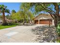 Wide driveway approaching a charming single-story home with a lushly landscaped yard and mature shade trees at 7508 E Aster Dr, Scottsdale, AZ 85260