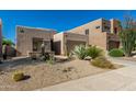 A tan home with xeriscaping and native plants, a stone facade, and an attached two-car garage at 10869 E Hedgehog Pl, Scottsdale, AZ 85262
