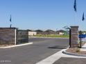 Gated Community entrance featuring well-maintained landscaping, stone pillars, black iron gates, and a playground in the background at 17417 W Eva St, Waddell, AZ 85355