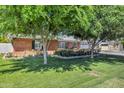 Well-maintained front yard with lush green grass, mature trees, and landscaped flower beds surrounding a charming brick home at 4634 E Wilshire Dr, Phoenix, AZ 85008