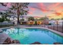 Backyard view of a refreshing in-ground pool surrounded by lush greenery and a secure fence at dusk at 5818 N 3Rd Ave, Phoenix, AZ 85013