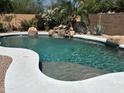 Beautiful swimming pool with a step entry surrounded by mature desert landscaping and a rock waterfall at 20426 N Alma Dr, Maricopa, AZ 85138