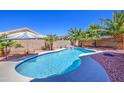 A private backyard oasis features a pristine pool, rock waterfall, and mature landscaping with palm trees at 43302 W Bunker Dr, Maricopa, AZ 85138