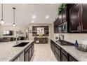 Open-concept kitchen with a large island, granite countertops, dark cabinets, and an adjacent living space at 2440 W Arroyo Way, San Tan Valley, AZ 85144