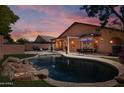 Relaxing backyard with a sparkling pool, rock waterfall feature, dining area, and lush greenery at 2236 E Rawhide St, Gilbert, AZ 85296
