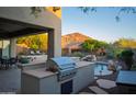 Outdoor kitchen area with stainless steel grill, pool views, natural landscaping, and mountain views beyond at 14045 E Geronimo Rd, Scottsdale, AZ 85259