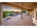 Covered brick patio overlooking a green view of the golf course at sunset with lush garden and mature trees at 22208 N San Ramon Dr, Sun City West, AZ 85375