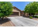 Home featuring a long driveway leading to a two-car garage, framed by desert landscaping and mature trees at 11952 W Overlin Ln, Avondale, AZ 85323