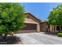 Home featuring a long driveway leading to a two-car garage, framed by desert landscaping and mature trees at 11952 W Overlin Ln, Avondale, AZ 85323