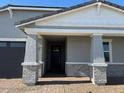 Inviting front entry with a covered porch featuring brick accents and a modern black front door at 17677 W Odeum Ln, Goodyear, AZ 85338