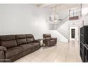 A bright living room with tile flooring, featuring a brown reclining sofa and view of the open staircase at 3134 E Mckellips Rd # 139, Mesa, AZ 85213