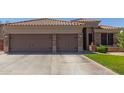 Inviting front view featuring a three car garage with brick accents, large driveway, and meticulously maintained landscaping at 20420 N 93Rd Dr, Peoria, AZ 85382